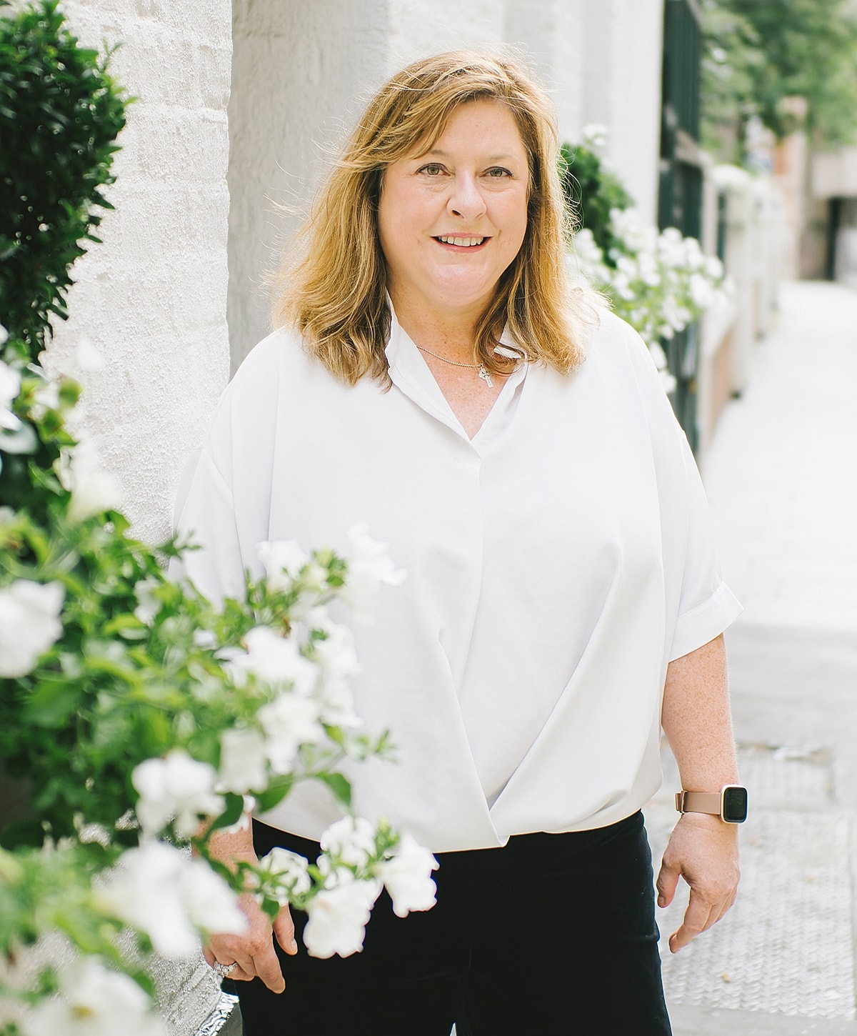 Woman standing outdoors near flowering plants.