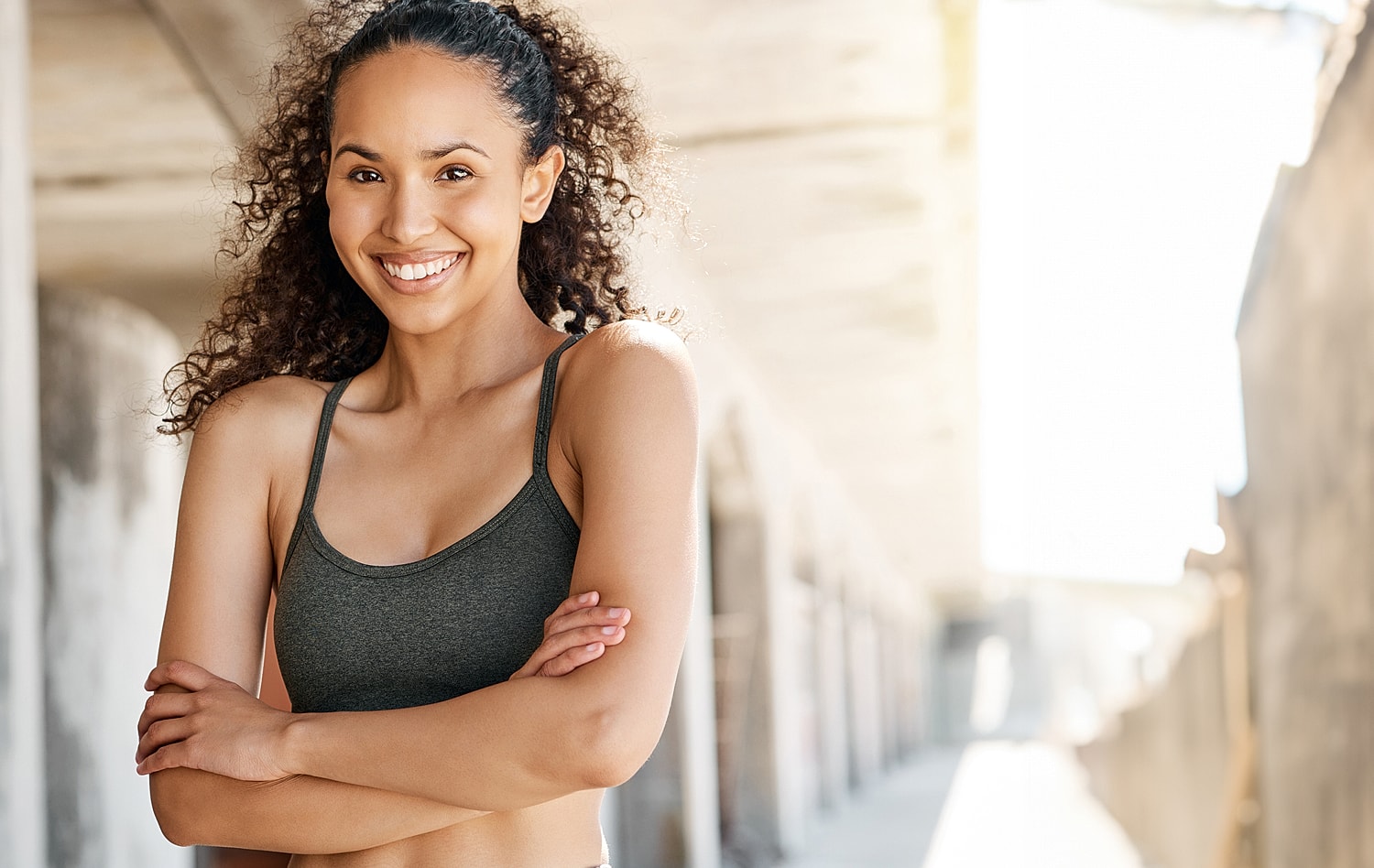 Smiling woman with curly hair indoors, arms crossed.