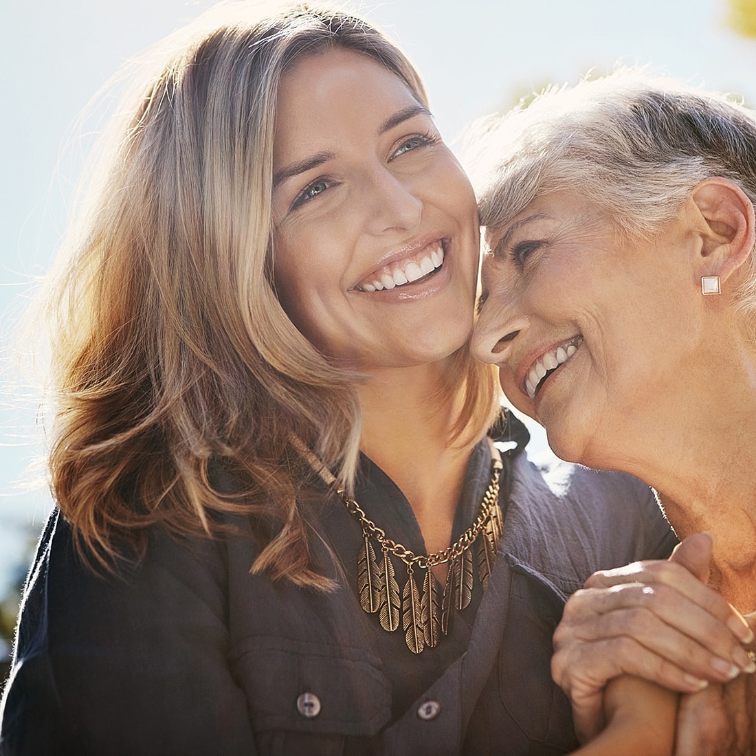 Smiling woman embraces her grandmother outdoors.