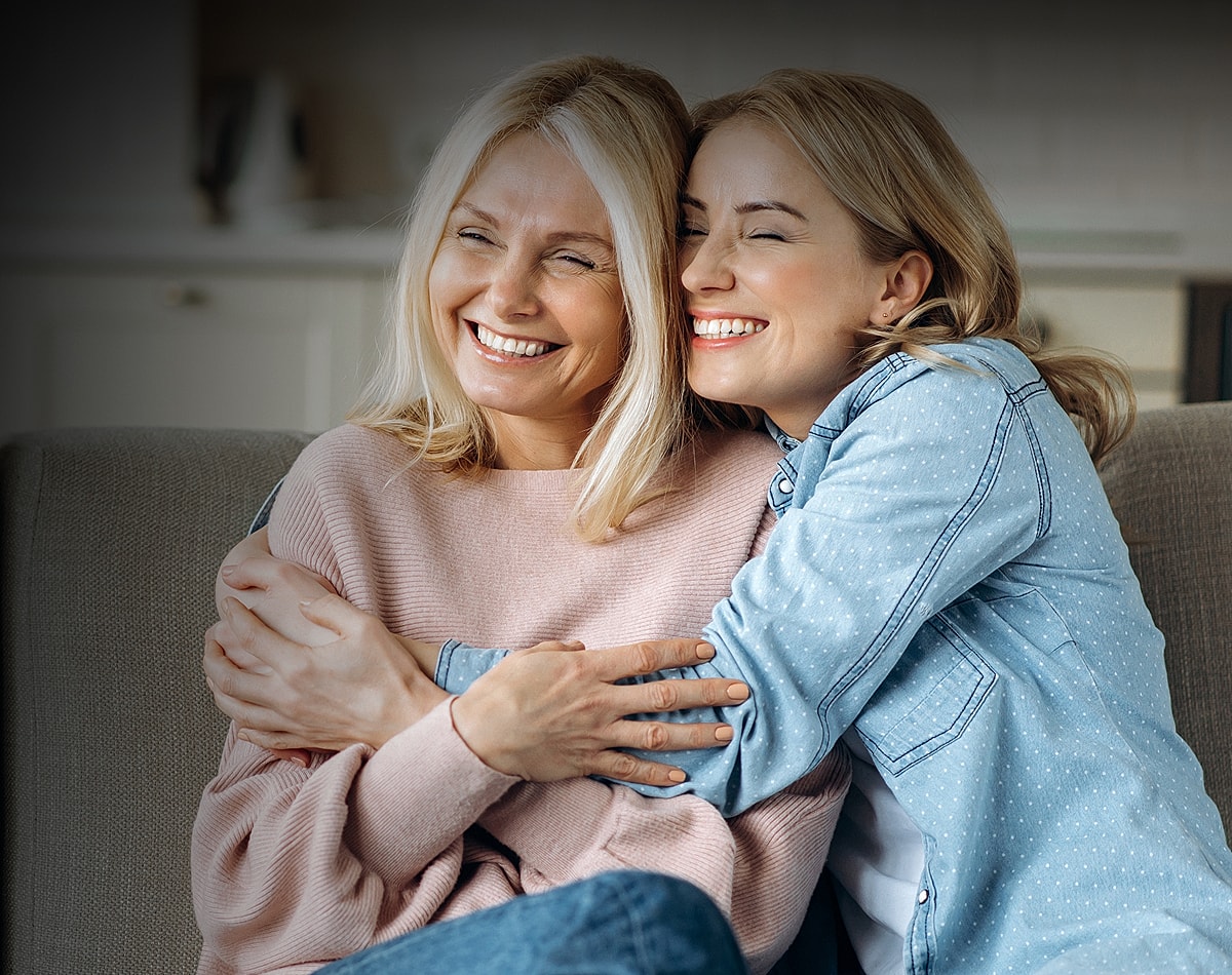 Two women smiling and embracing on a sofa.